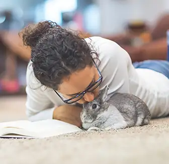 Junge Frau liegt neben ihrem Kaninchen und liest in einem Buch