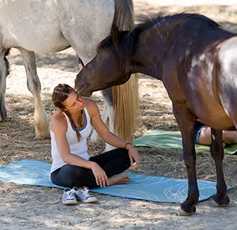 junge Frau mit Yogamatte bei einer Gruppe von Pferden