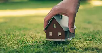 Modellhaus wird von einer Hand auf die Wiese gestellt