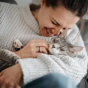 Eine Frau, die mit ihrer Katze kuschelt und lächelt.