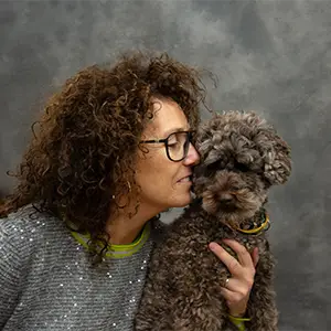 Frau mit lockigem Haar, die ihren Hund küsst.