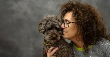 Frau mit lockigem Haar, die ihren Hund küsst.