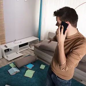 Mann telefoniert in seiner ausgeräumten Wohnung mit der Versicherung