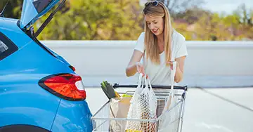 Frau verstaut die Einkäufe im Kofferraum