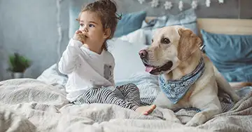 Kleines Mädchen sitzt neben dem Hund im Bett